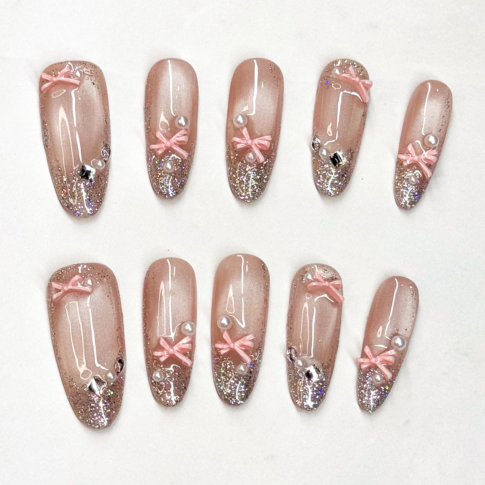 • Glitter Glam: Nude-to-sparkle gradient for a dazzling effect.
• 3D Ribbon Charm: Baby-pink bows add playful elegance.
• Pearl &amp; Gem Accents: Tiny luxe details that catch the light.
• Long oval Shape: Slim, flattering silhouette for all occasions.
• Handmade &amp; Reusable: Durable, salon-quality press ons.