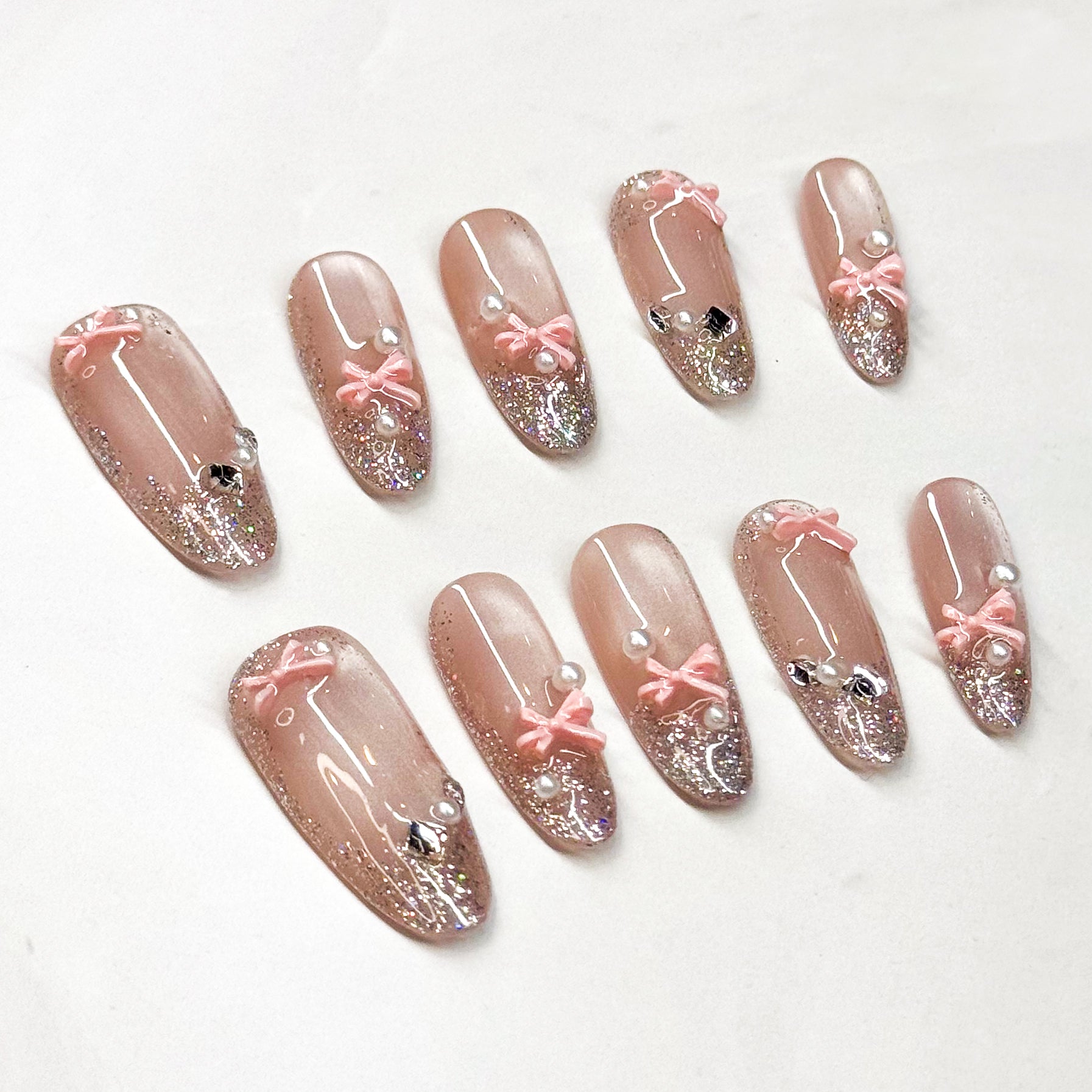 • Glitter Glam: Nude-to-sparkle gradient for a dazzling effect.
• 3D Ribbon Charm: Baby-pink bows add playful elegance.
• Pearl &amp; Gem Accents: Tiny luxe details that catch the light.
• Long oval Shape: Slim, flattering silhouette for all occasions.
• Handmade &amp; Reusable: Durable, salon-quality press ons.