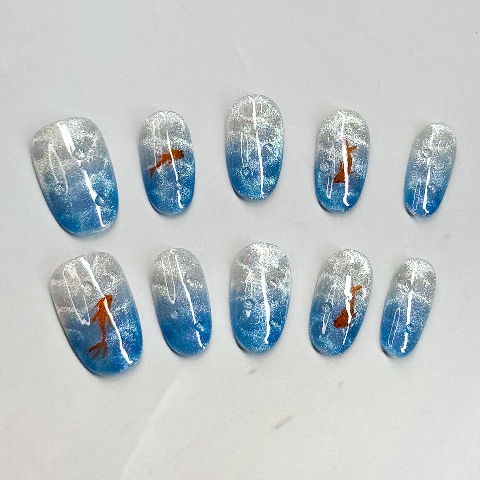 • Serene Gradient: Blue and silver shimmer mimic sparkling water.
• Artistic Touch: Orange koi fish bring movement and charm.
• Minimal &amp; Elegant: A balance of simplicity with subtle detail.
• Medium Oval Shape: Natural and wearable for everyday style.
• Handmade &amp; Reusable: Crafted with salon-quality gel for durability.