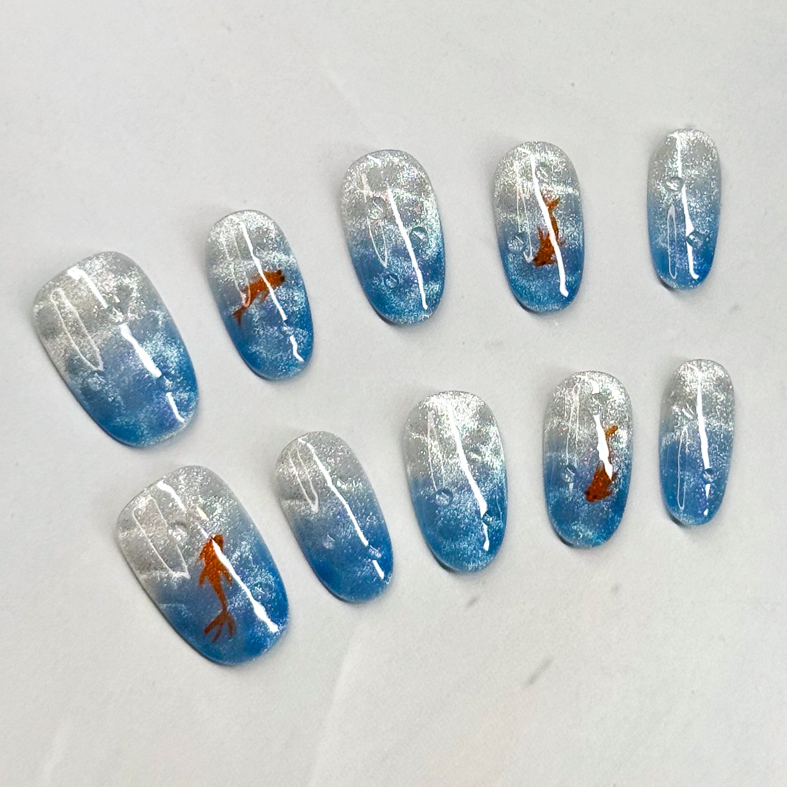 • Serene Gradient: Blue and silver shimmer mimic sparkling water.
• Artistic Touch: Orange koi fish bring movement and charm.
• Minimal &amp; Elegant: A balance of simplicity with subtle detail.
• Medium Oval Shape: Natural and wearable for everyday style.
• Handmade &amp; Reusable: Crafted with salon-quality gel for durability.