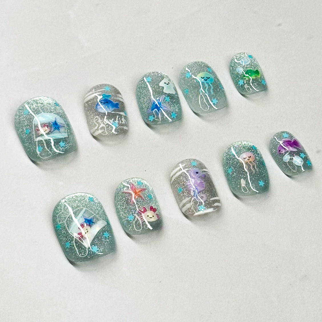 • Sparkling Base: Glittery aqua + silver backdrop with a dreamy ocean glow.
• Sea Life Accents: Whimsical marine designs — seahorse, jellyfish, dolphins, and more.
• Cute & Playful: Fun pops of color like purple, coral, and blue for a lively touch.
• Short Square Shape: Easy to wear and practical while still eye-catching.
• Handmade & Reusable: Crafted with 3D gel for durability and reusability.