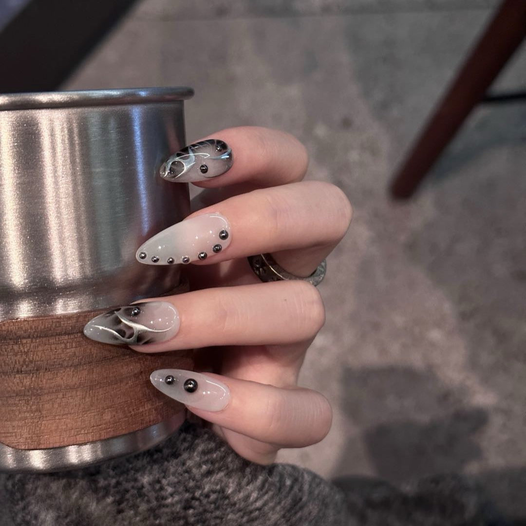Unleash a bold, futuristic edge with Obsidian Chrome Press-On Nails. This striking set features a smoky gray base with sleek black chrome flame designs, accented by metallic studs for a modern, industrial-inspired aesthetic. The combination of glossy and matte finishes, along with sculpted 3D elements, creates a daring and sophisticated look that’s perfect for trendsetters who love an avant-garde touch.