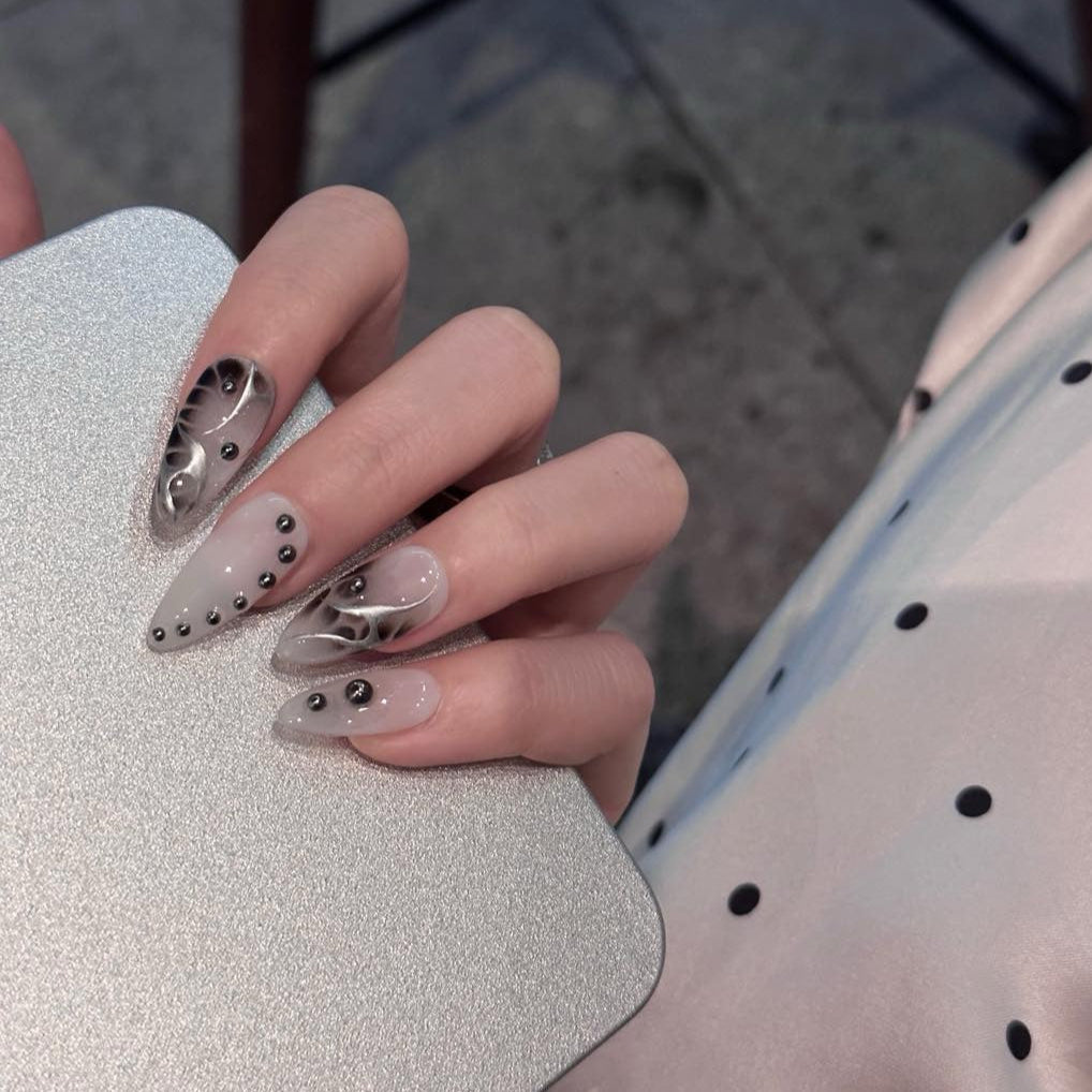 Unleash a bold, futuristic edge with Obsidian Chrome Press-On Nails. This striking set features a smoky gray base with sleek black chrome flame designs, accented by metallic studs for a modern, industrial-inspired aesthetic. The combination of glossy and matte finishes, along with sculpted 3D elements, creates a daring and sophisticated look that’s perfect for trendsetters who love an avant-garde touch.