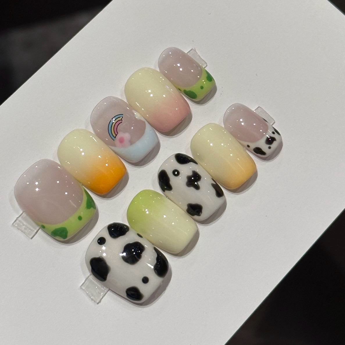 Step into a whimsical world with Pastel Pasture Press-On Nails, a playful blend of rainbow accents, cow prints, and pastel gradients. This charming set captures the essence of a dreamy countryside with its short square shape and glossy finish, featuring a delightful mix of green clover patterns, sunset ombré, and adorable cow spots. Perfect for adding a touch of fun and fantasy to your everyday look, Pastel Pasture brings a cute, nostalgic vibe to your nails.