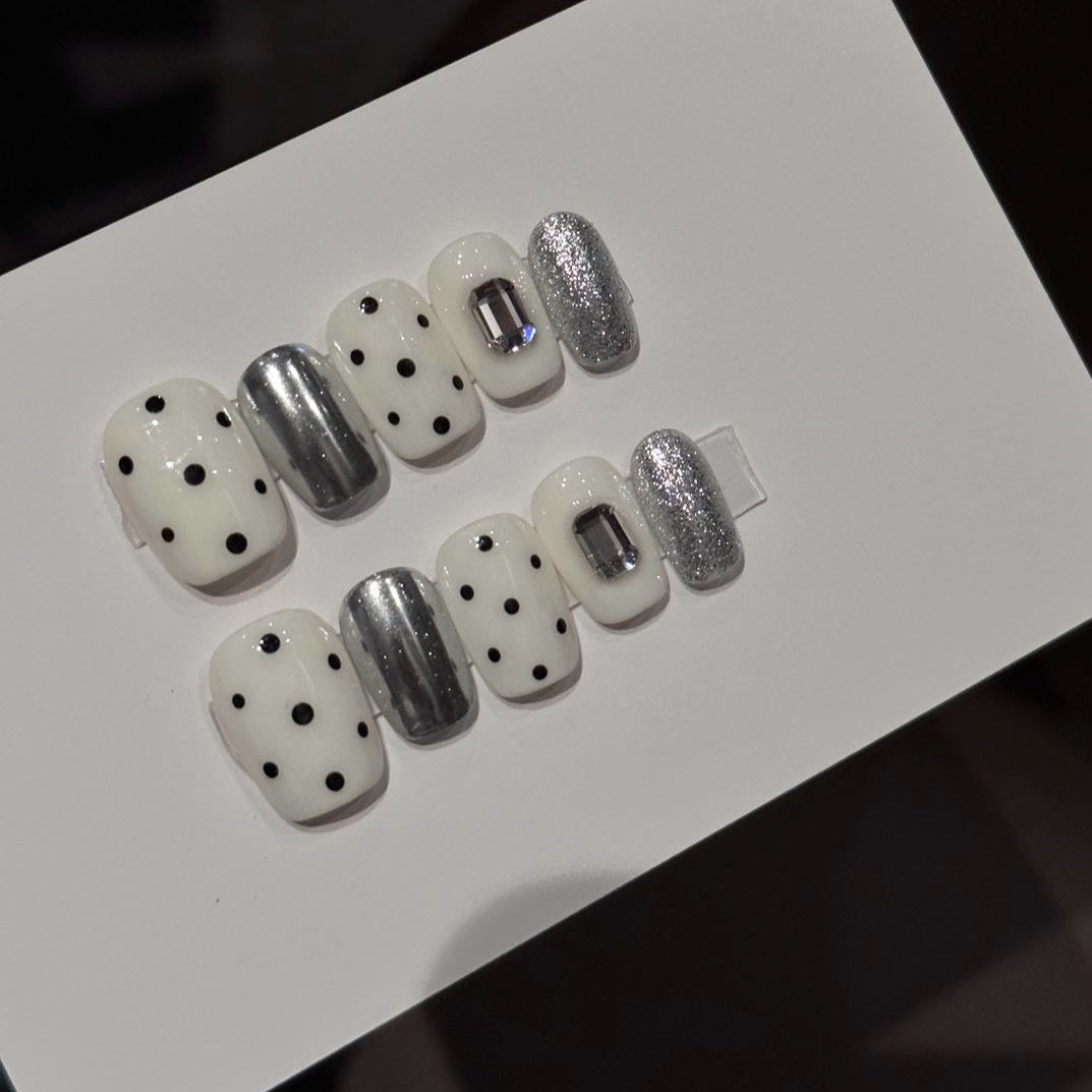 Break the rules of classic style with Polka Punk Chic Press-On Nails, a bold and playful combination of monochrome polka dots, metallic silver accents, and geometric embellishments. This eye-catching set features a short square shape with a glossy finish, blending retro charm with a futuristic edge. Perfect for those who dare to stand out, Polka Punk Chic brings a playful yet rebellious statement to your nails.