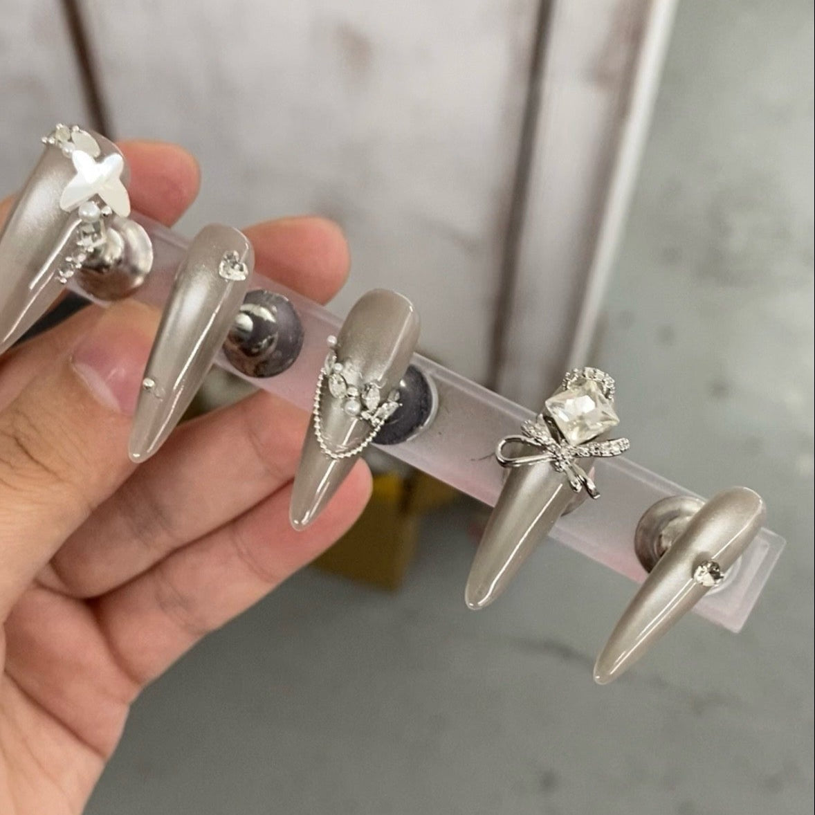 Embrace luxury and elegance with the Silver Luster Press-On Nails. This dazzling set combines shimmering silver tones, delicate rhinestone embellishments, and regal bow-shaped gems to create a sophisticated and glamorous look.