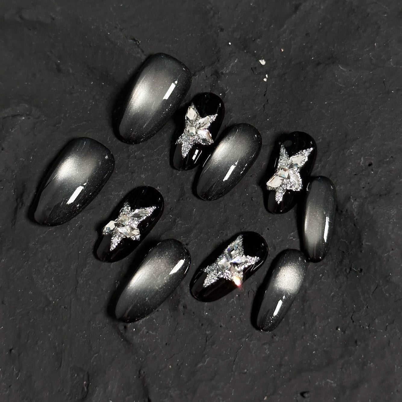 Starlit Shadows Press-On Nails capture the mystique of a starry night sky with a mesmerizing cat-eye effect that shimmers like cosmic dust. Accented with 3D silver star embellishments, these nails create a celestial and ethereal vibe that’s both elegant and edgy.