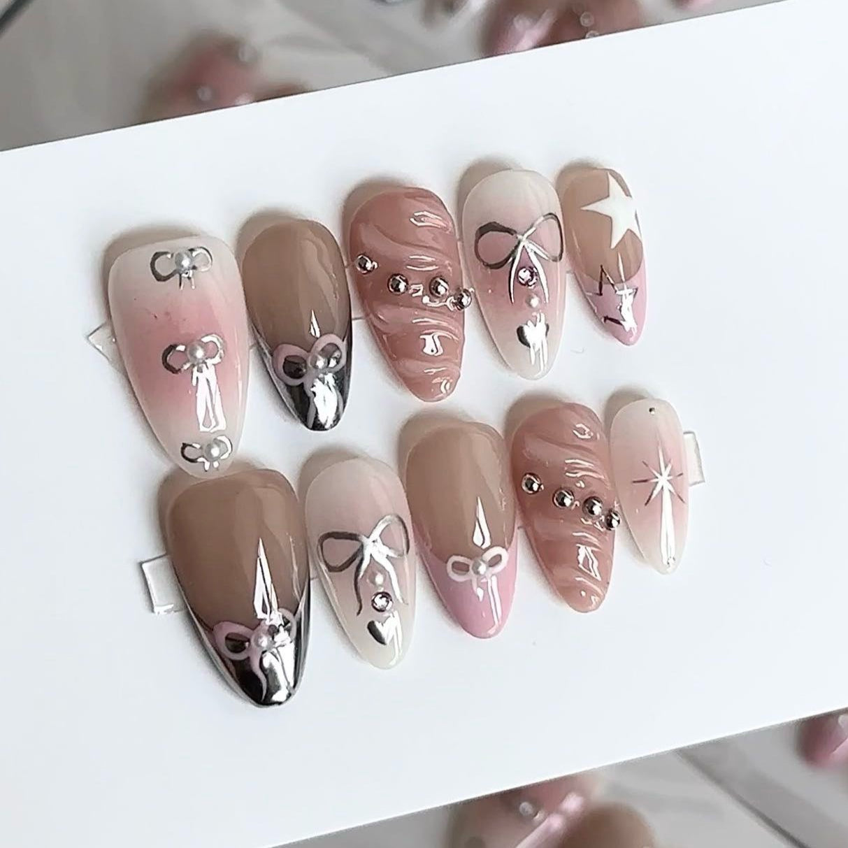 Embrace charming elegance with Whimsical Bows Press-On Nails, a delightful blend of soft blush pink, taupe, and delicate silver accents. This playful set features adorable bow designs, shimmering star motifs, and subtle rhinestone embellishments, capturing a whimsical, fairytale-inspired look. With a glossy finish and graceful almond shape, Whimsical Bows adds a touch of feminine sweetness to your style.